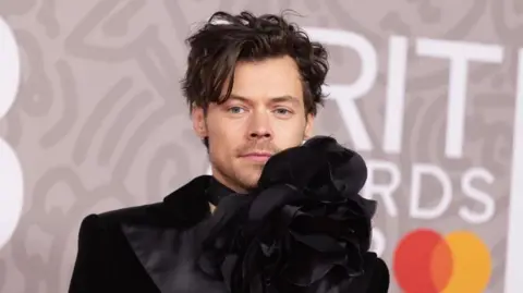 Getty Images Harry Styles in a black designer jacket with over-sized flower detail at his neck, at the Brit Awards