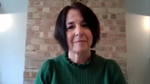 Andrea Brady, who has short dark brown hair, wears a green cable knit jumper and speaks to BBC Breakfast over a Zoom link from her home
