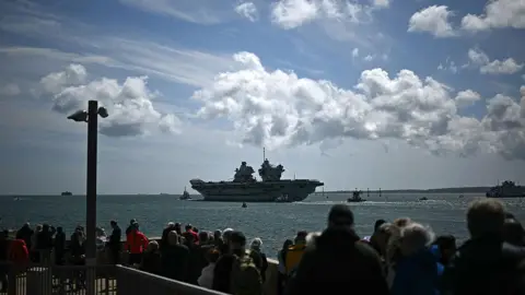 Getty Images A British aircraft carrier is watched by crowds as it sails.