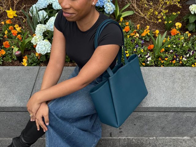 Editor sitting outside by flowers with the Kaai Midi Pyramid tote in teal