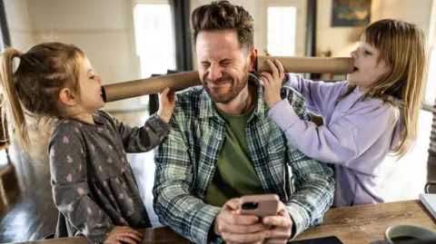 Getty Images A dad trying to work from home while two young daughters are playfully yelling in his ears