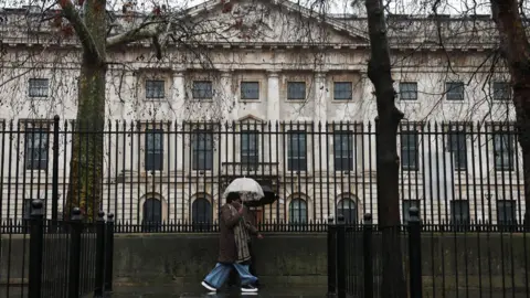 Reuters A woman holding an umbrella past black railings in front of the Royal Mint Court, the proposed site of the new Chinese embassy in London.