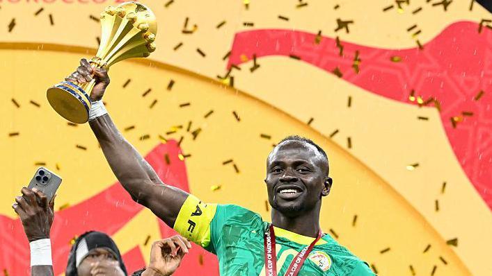 Sadio Mane smiling and holding the Africa Cup of Nations trophy up