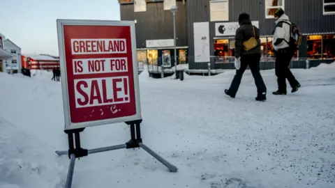 EPA/Shutterstock People walk along an icy street in Nuuk, Greenland's capital. A sign on the street says: "Greenland is not for sale!"