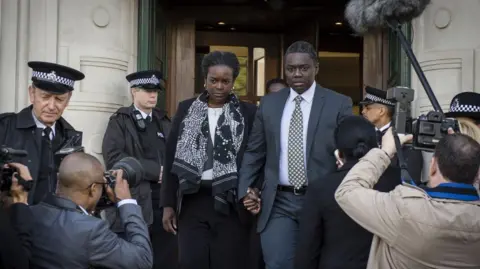 Minnow Films The characters of Gloria Taylor, played by Wunmi Mosaku and Richard Taylor, played by Babou Ceesay, are pictured leaving a courthouse surrounded by police officers and photographers during the drama.