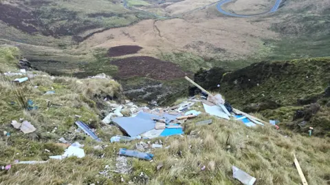 Nathan Dixon A view of the dumped waste on the mountain looking down on the valley below. A winding road can be seen in the distance.