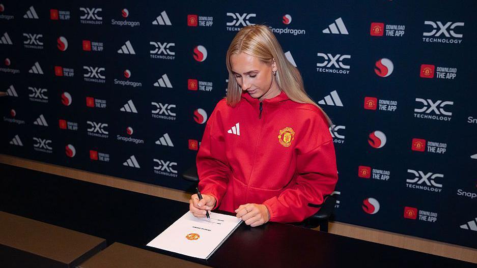 Ellen Wangerheim, in a red Manchester United tracksuit top, signing a contract