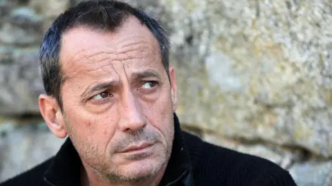 AFP A man in a black sweater looks askance with a short beard and greying hair