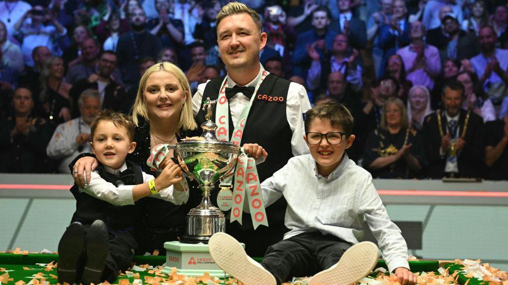 Kyren Wilson, Sophie Wilson and their sons stand around the World Championship trophy