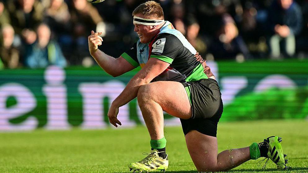 Fin Baxter kneels down and throws the ball in the air after scoring a try for Harlequins