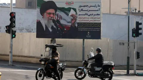EPA Motorcyclists drive past a billboard showing Iran's Supreme Leader Ayatollah Ali Khamenei and a quote accusing US President Donald Trump of fomenting the recent deadly unrest (24 January 2026)