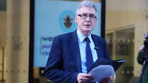 PA Media PCC Simon Foster wears a suit while reading from a file outside of his office.