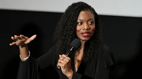 Getty Images Nia DaCosta gesturing as she speaks into a microphone