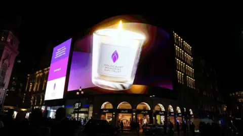 PA Media A large digital screen at Piccadilly Circus shows a candle which reads 'Holocaust Memorial Day Trust' against a purple background.