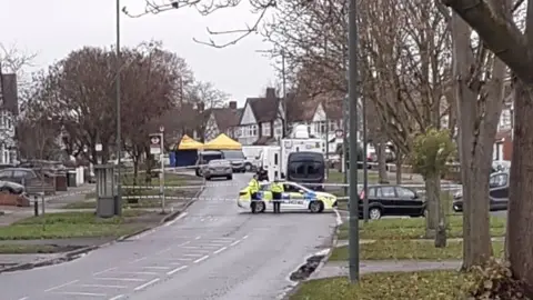 @andyclay4 Yellow forensic tents, explosives team vans and a police car and cordon on Willersley Avenue, a residential street lined with trees