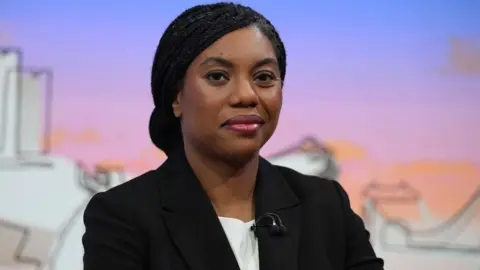 Jeff Overs/BBC Kemi Badenoch appearing on the Laura Kuenssberg wearing a black blazer and white blouse against a colourful backdrop