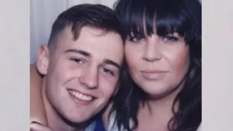 Nicola Howarth A passport-booth style photograph showing Alfie and his mother with their heads close together as they smile at the camera.  Alfie has short brown hair, with a curl that falls onto his forehead. Nicola has black, wavy hair, with a heavy fringe.