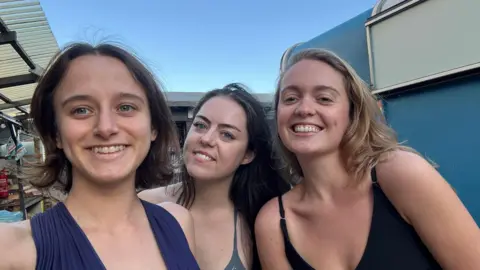 Ana Cass Head and shoulders of Ana (left) with two friends outside a sauna.