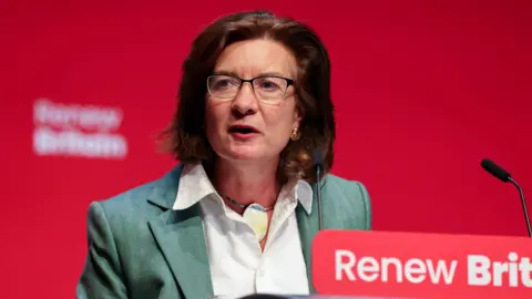 Reuters Eluned Morgan stood addressing a Labour conference, wearing a green jacket and open necked white shirt.