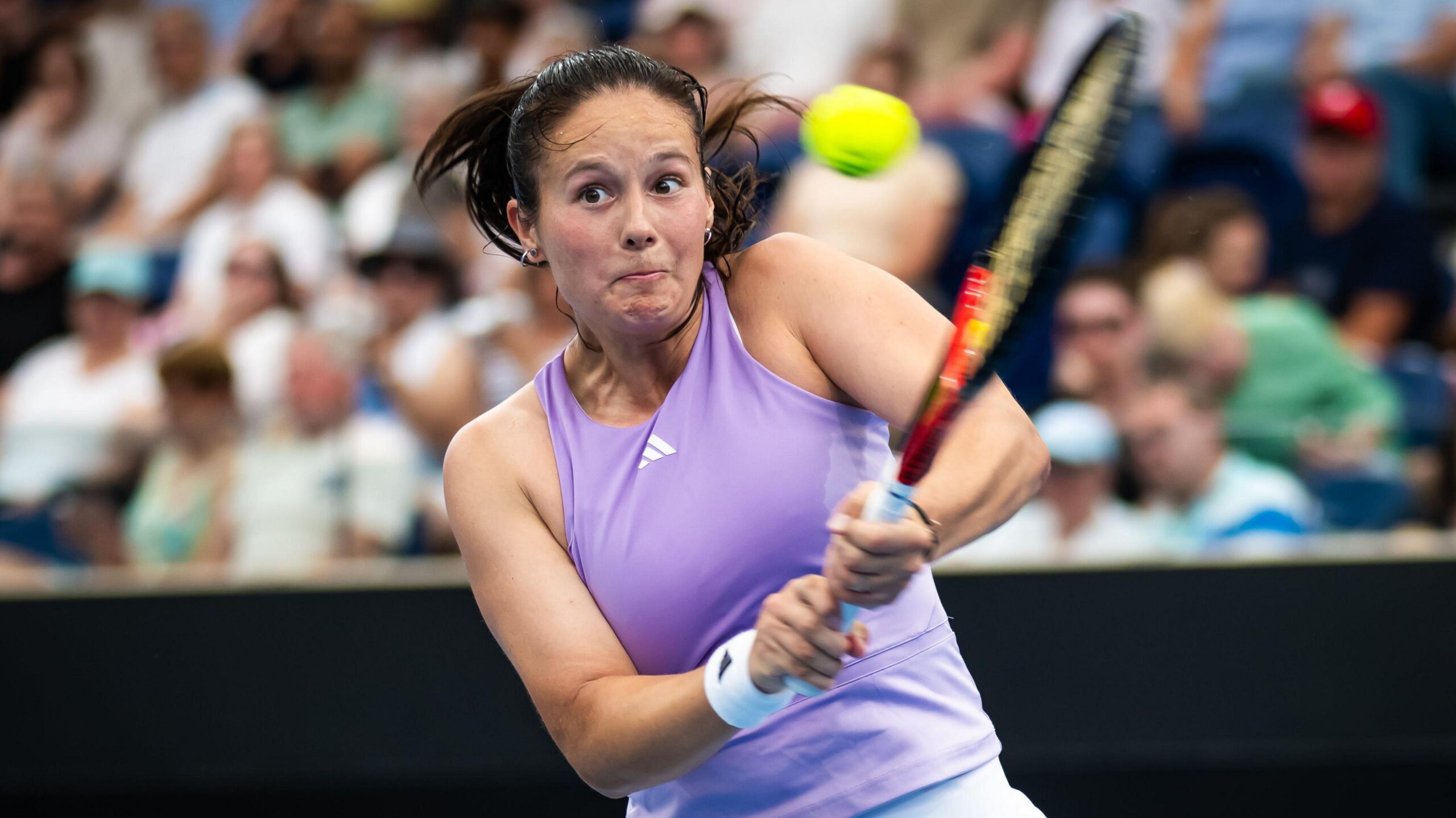 Daria Kasatkina, in a lilac tennis vest, plays a two-handed backhand shot as her eyes suggest intense focus