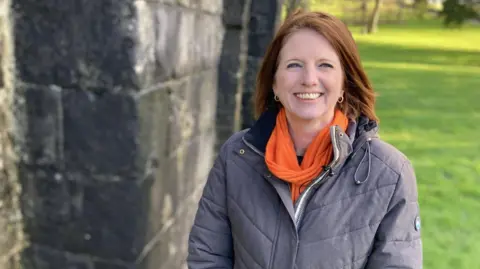 Harriet Eaton, Heritage Education Officer at Neath Port Talbot Council stands in Margam park wearing a grey coat and an orange scarf. It is a head and shoulders shot of her.