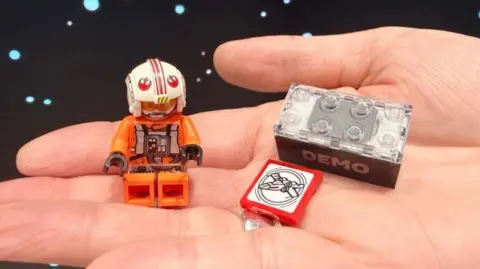 The Smart Minifigure, Smart Brick and Smart Tag shown together resting on the palm of someone's hand.