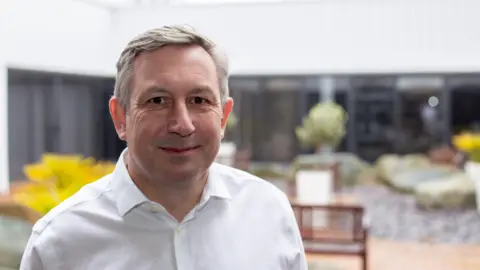 FireAngel Wearing a smart, white shirt, Nick Rutter smiles at the camera.