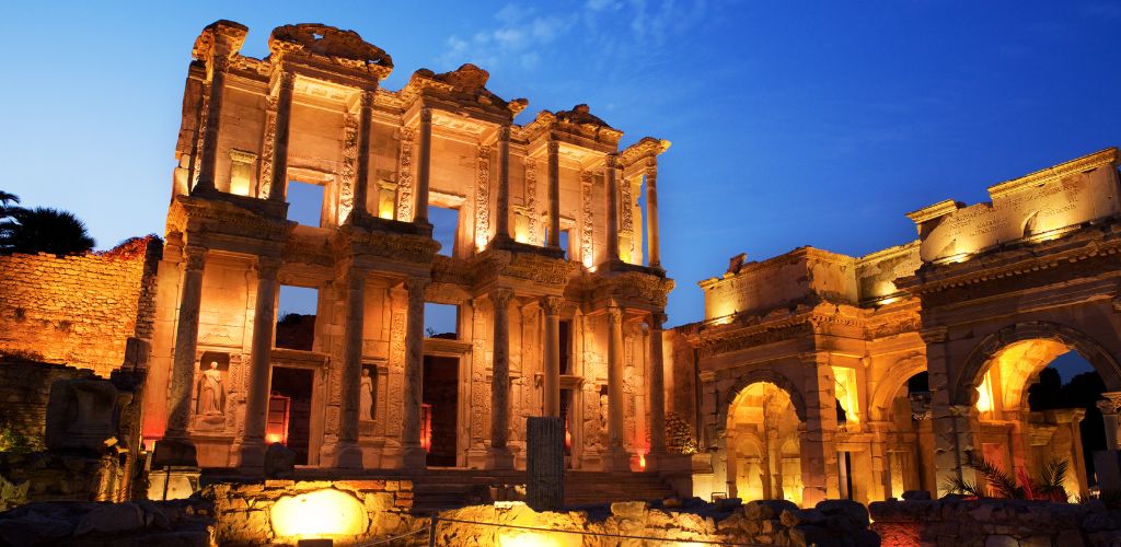 An image of Ephesus's historical structure at night and has a yellow dim light around.