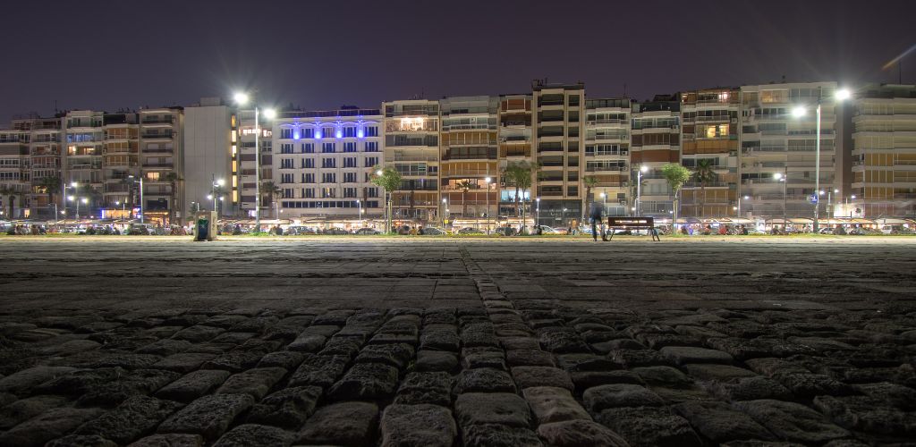 At night, there are buildings, one bench, and a road made by stone.