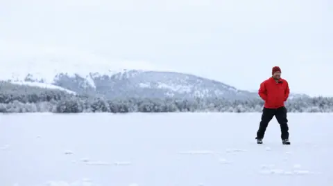 Reuters A man wearing a red jacket stands to the right of the frame - the ground is covered in ice and snow