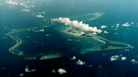 Reuters An aerial view of Diego Garcia, the largest island in the Chagos archipelago. Fluffy white clouds are above the island, which is surrounded by deep blue water.
