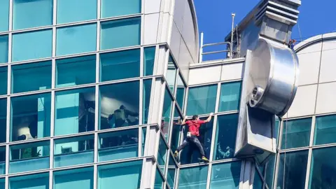 Getty Images US rock climber Alex Honnold scales the Taipei 101 building without ropes or safety gear. He is wearing black trousers and a red t-shirt.