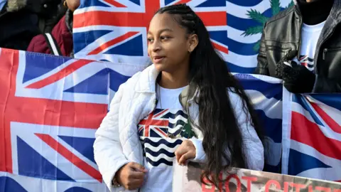 Alamy A woman wearing a t-shirt bearing the flag of the British Indian Ocean Territory takes part in a protest against the UK-Mauritius Chagos Islands deal outside the UK Parliament in January 2026.