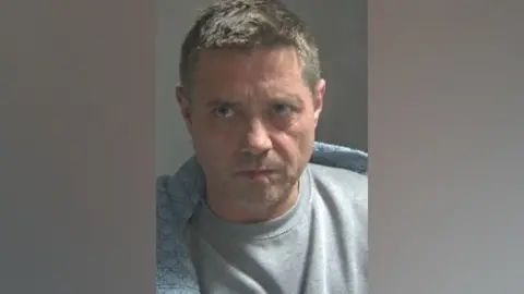 Hertfordshire Constabulary A mugshot of John Alford wearing a grey T-shirt.