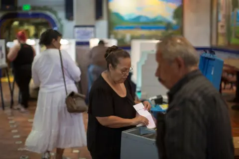 Getty Images Woman holding ballot paper near voting station with another man in foreground
