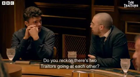 Harry and Zack next to each other at the roundtable with Harry asking Zack "Do you reckon there's two Traitors going at each other?"