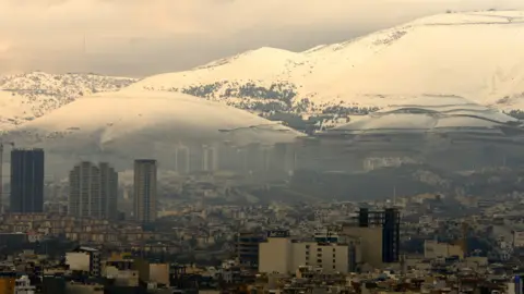 Fred Scott/BBC The view of Iran from the border of Iraqi Kurdistan, with buildings and tower blocks in the foreground and snow-covered mountains in the background