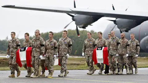 Getty Images Danish troops carry two coffins draped in the national flag from a cargo plane. The troops are wearing military uniforms with black armbands.
