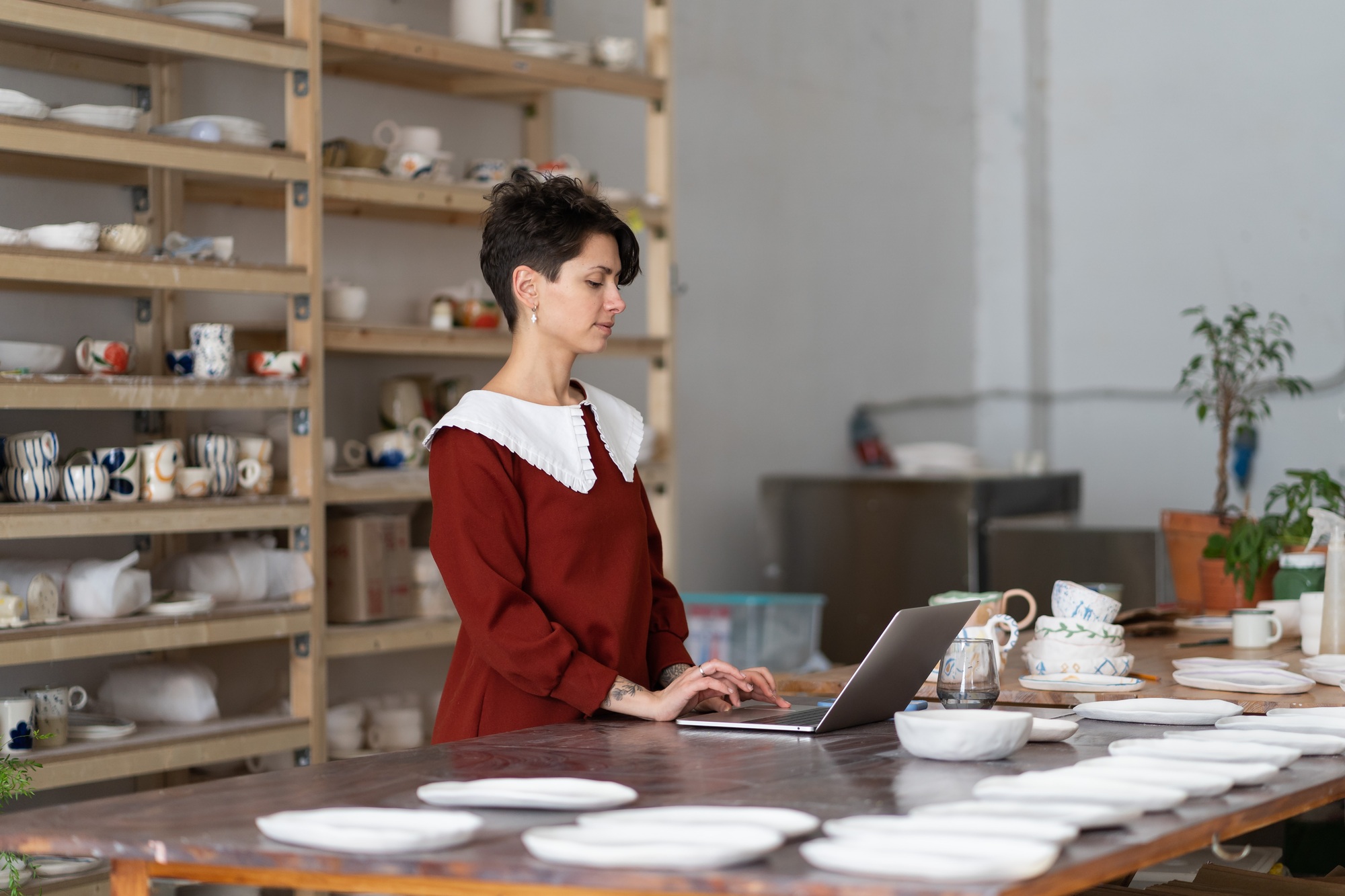 Craftswoman using laptop to sell handmade pottery items through online marketplaces