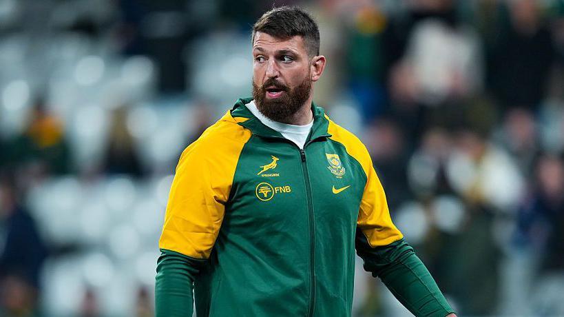 Jean Kleyn wearing South Africa training leisure kit, walking on the pitch while looking over his right shoulder before a match for the country