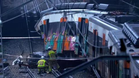 EPA Firefighters are seen on a train track next to the derailed carriage of a commuter train near Barcelona
