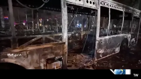 Islamic Republic of Iran Broadcasting via WANA via Reuters A burnt-out bus lies on the road at night in this screen grab from Iran's state-media broadcast footage. The central door is no longer attached to the vehicle. Charred remains of seats are inside.