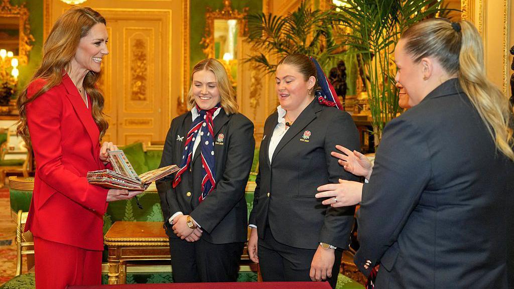 The Princess of Wales holds a book and speaks with three England players