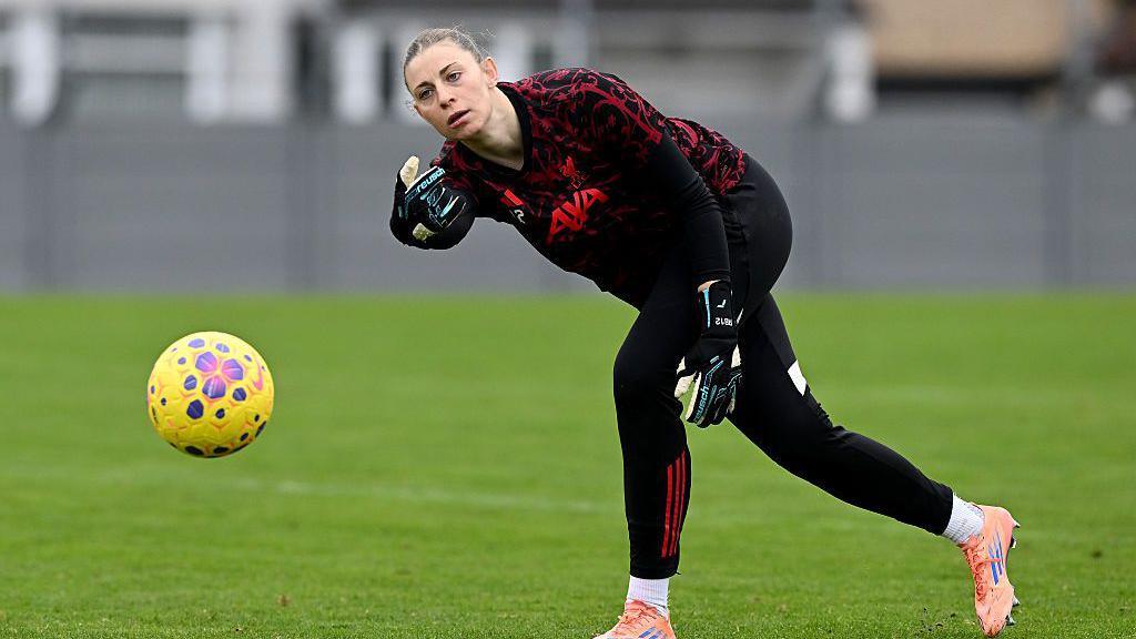 Rafaela Borggrafe rolls a yellow football while wearing black and red goalkeeper kit