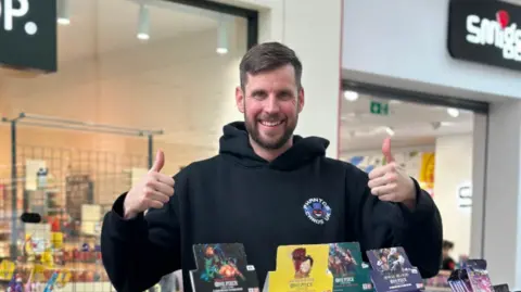 Lee Fowler Lee Fowler with two thumbs up with cards in front of him