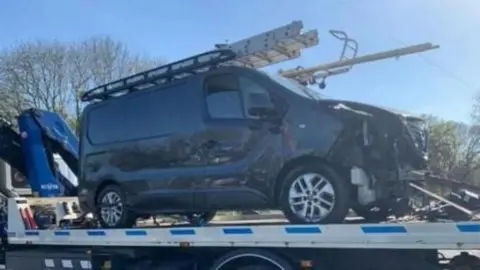 A tow truck with a smashed grey van loaded on to it