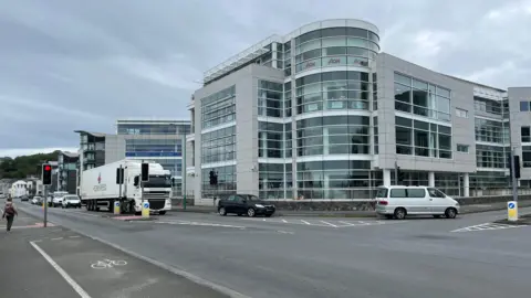 Admiral Park in Guernsey - Large grey buildings on a corner next to traffic lights, with lots of windows.