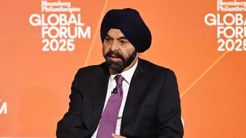 Getty Images An image of Ajay Banga speaking in front of an orange backdrop, while dressed in a black turban and black suit with a purple tie.