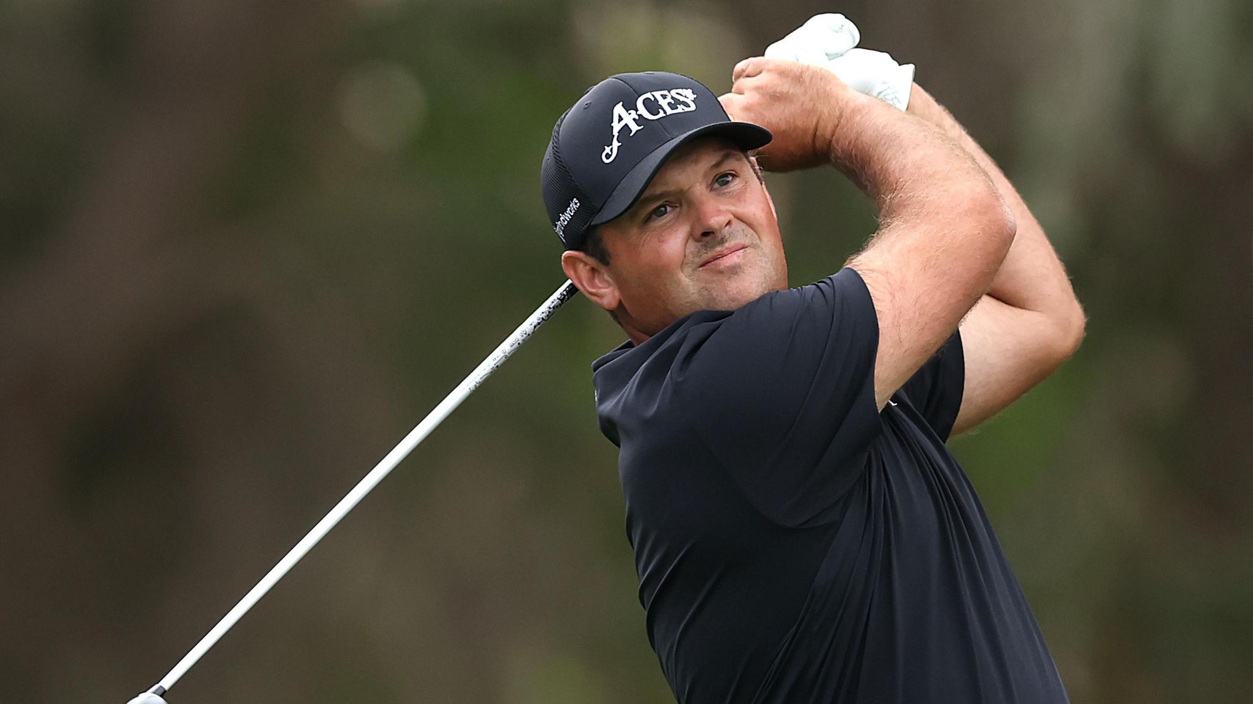 Patrick Reed, dressed in black, watches his ball after a shot