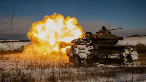 Roman Chop/Global Images Ukraine via Getty Images A large blast of white and orange flame coming from a Ukrainian tank, as it fires towards Russian positions in a snowy landscape in the Donetsk region in January 2024